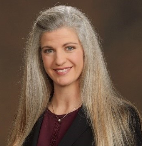 Woman with light-colored hair and grey eyes named Lynn Van Male wearing a black blazer and maroon top
