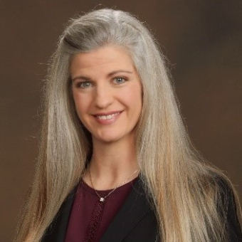 Woman with light-colored hair and grey eyes named Lynn Van Male wearing a black blazer and maroon top
