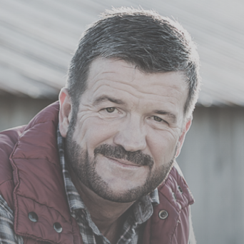 Man smiling leaning on fence in a rural setting